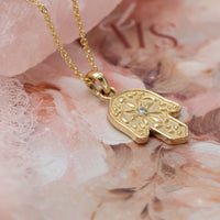 Gold Hamsa pendant necklace with a diamond on a floral background