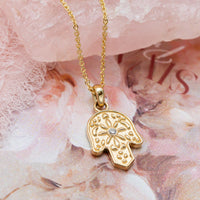 Gold Hamsa pendant necklace with a diamond on a floral background