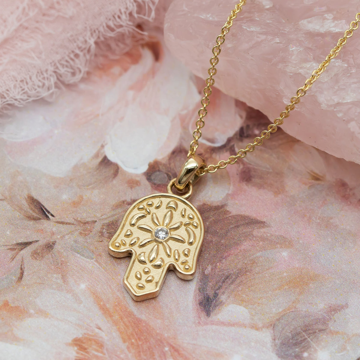 Gold Hamsa pendant necklace with a diamond on a floral background