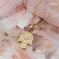 Gold Hamsa pendant necklace with a diamond on a floral background