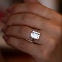 Large rose quartz pink gemstone ring on the finger, step-cut stone in a gold four-prong setting