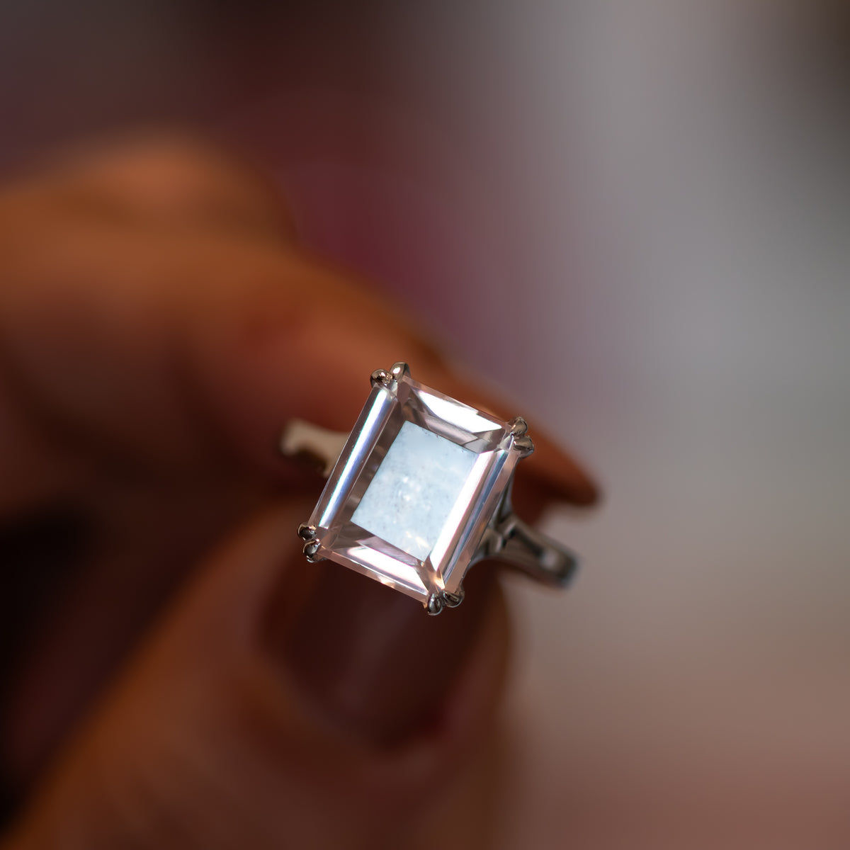 Rose quartz cocktail ring worn on hand, emerald-cut pink stone in a polished gold setting