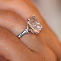 Rose quartz ring held up to show the split-shoulder band and diamond-lined crossover gallery