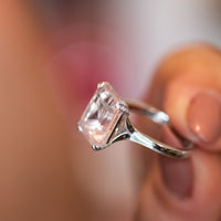 Rose quartz ring held up to show the split-shoulder band and diamond-lined crossover gallery
