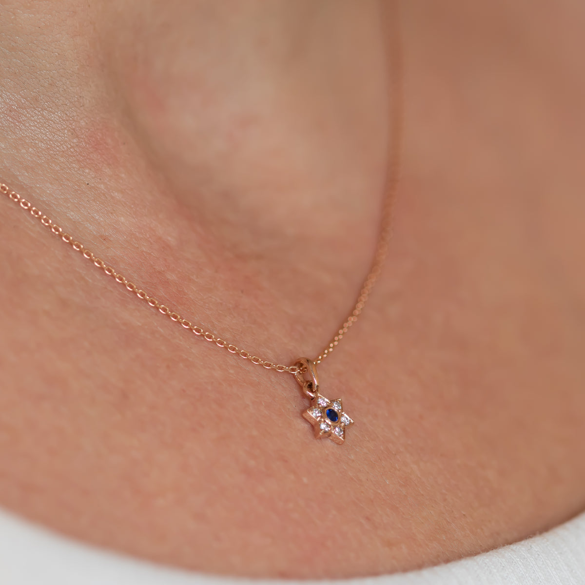 Small Star of David Charm necklace with blue sapphire and diamonds in 14k rose gold on neck