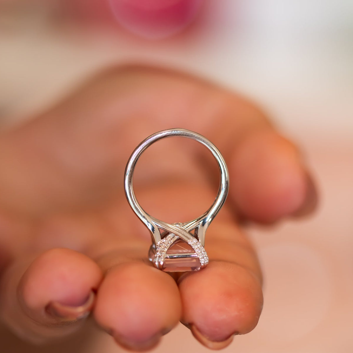 Rose quartz ring held up to show the split-shoulder band and diamond-lined crossover gallery