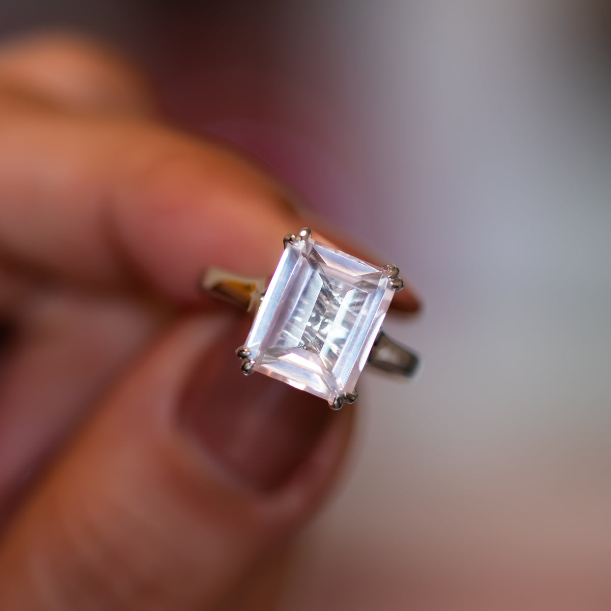 Verena rose quartz ring held to the light, large step-cut pink rose quartz in a four-prong gold setting
